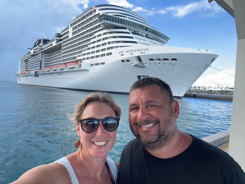 Man and woman taking a selfie in front of a cruise ship