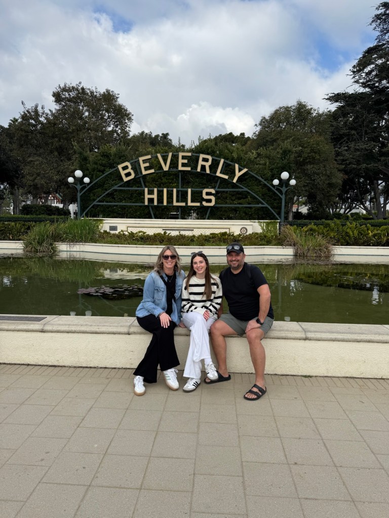 Family sitting on the edge of a fountain in front of a Beverly Hills sign