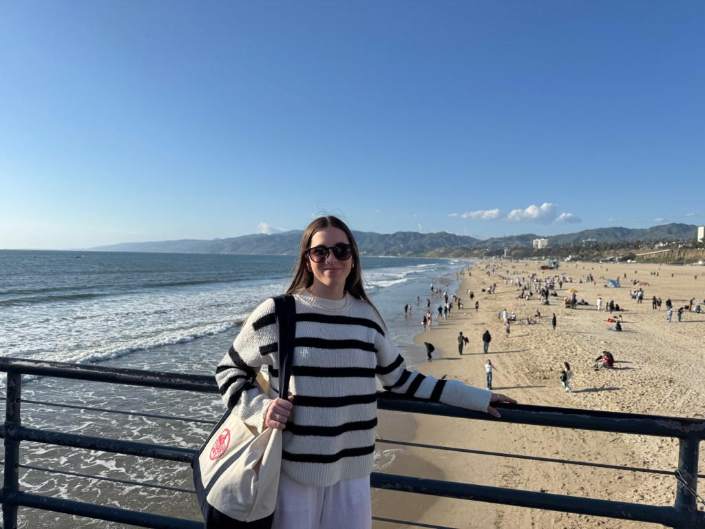 Young woman standing by a railing with a beach and ocean in the background