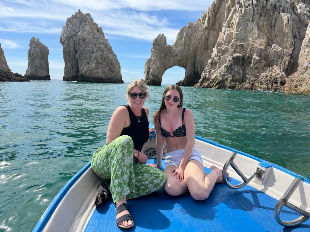 Mother and daughter sitting on the bow of a boat in front of rock formations in Cabo San Lucas