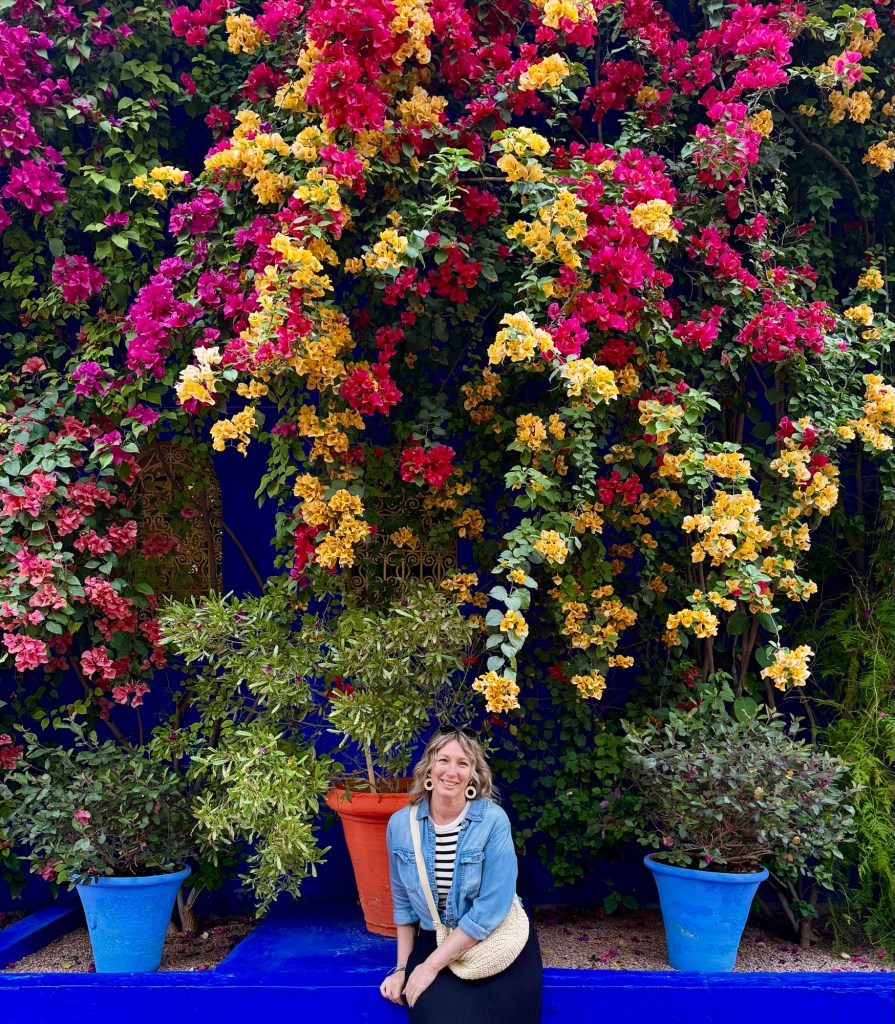 Woman sitting in front of a wall of beautiful colourful flowers 