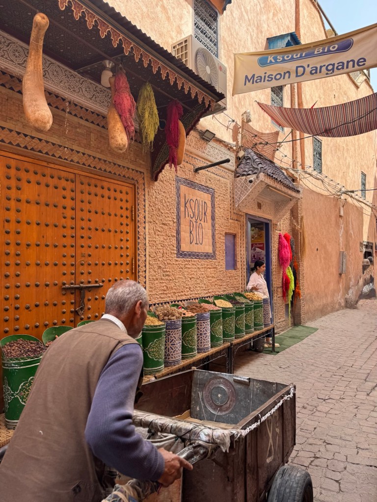 Man pushing a cart in front of a market stand selling flowers and herbs