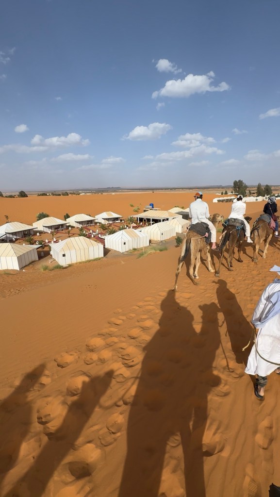Caravan of camels and riders arriving at a tent camp in the desert
