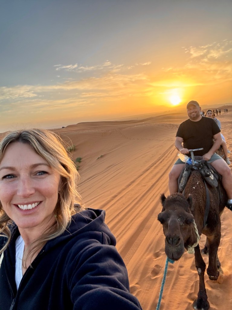 Man and woman riding camels in the desert at sunrise