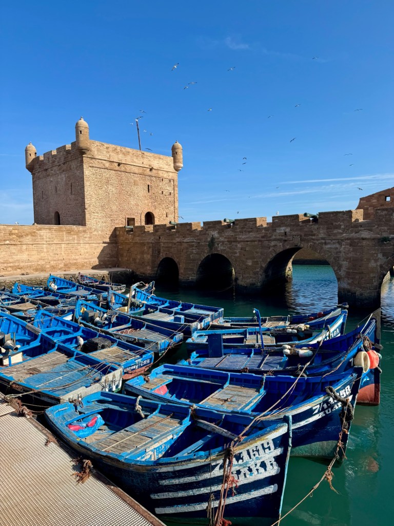 Blue boats in the water in front of a stone fortress